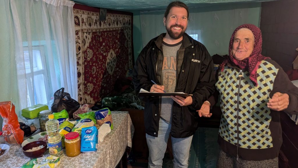 A Peace Corps volunteer with an elderly woman and all the food from the package spread out on a table.