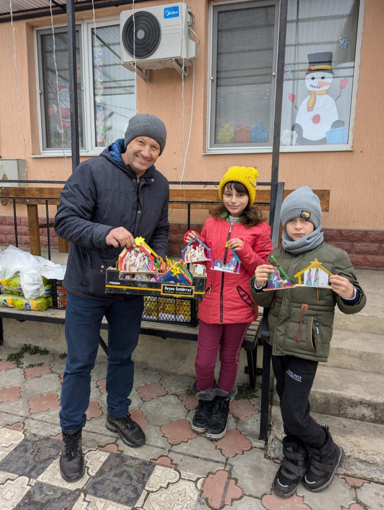 Victor with two children outside the community center, posing with gifts for the elderly