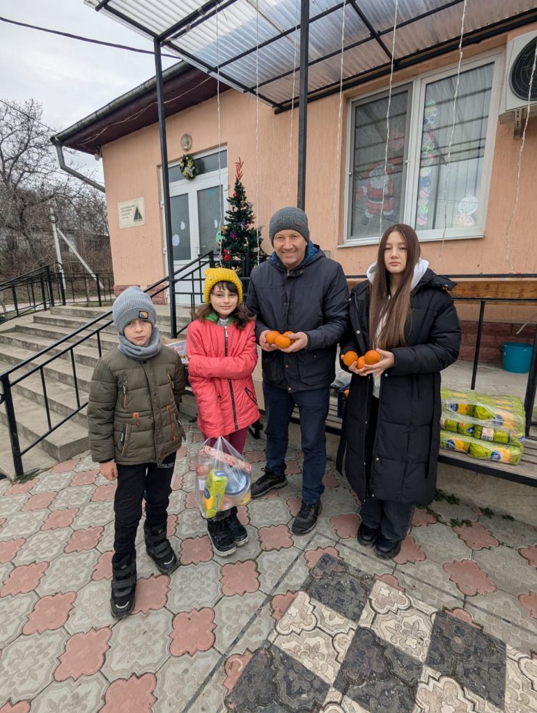 Victor, a volunteer, and two children posing outside the community center with mandarines for the elderly