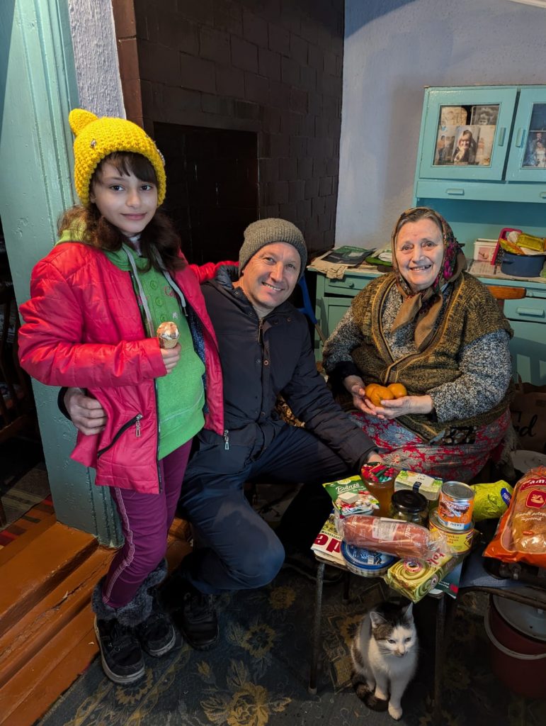 Victor, a child, and one elderly beneficiary posing with the food delivery.