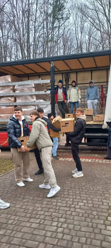 Smiling teenagers unloading the gifts from the semi-truck with the help of Peace Corps Volunteer Adam.