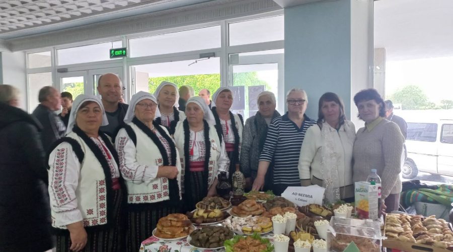 The ladies from the Seniors Club wearing traditional garb along with Victor in front of a table full of traditional foods that they made.