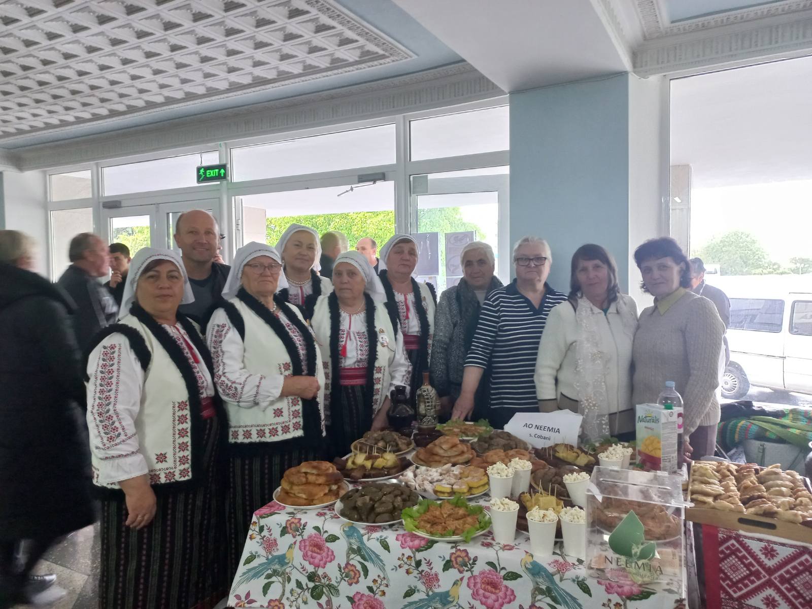 The ladies from the Seniors Club wearing traditional garb along with Victor in front of a table full of traditional foods that they made.