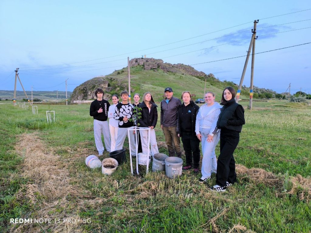 Volunteers and Mr. Victor posing in front of a planted tree with their buckets for water.