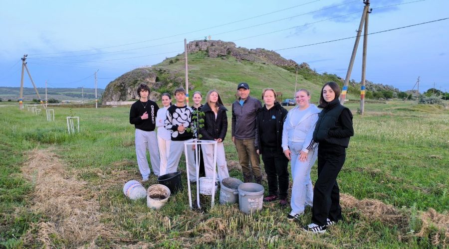 Volunteers and Mr. Victor posing in front of a planted tree with their buckets for water.