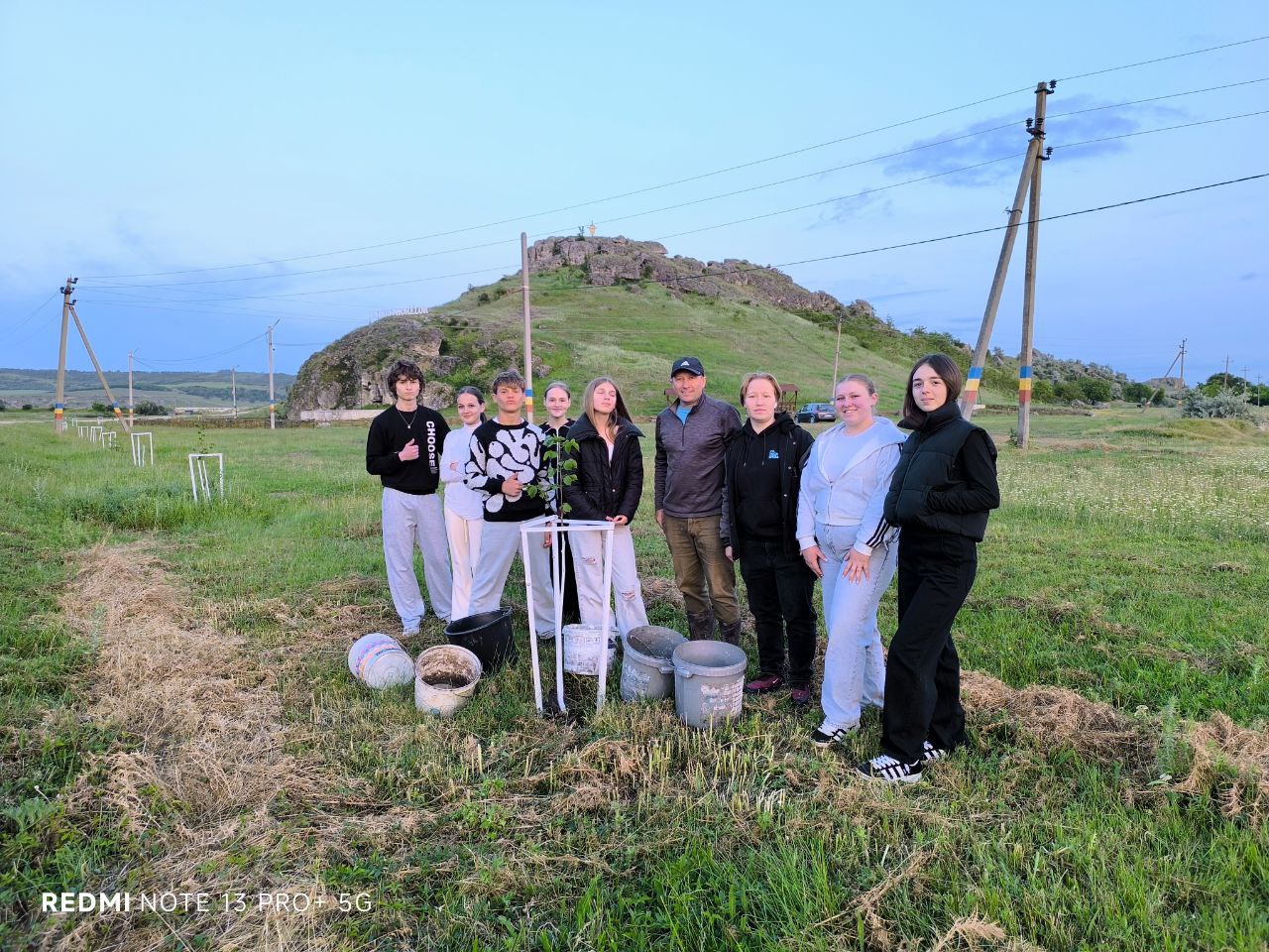 Volunteers and Mr. Victor posing in front of a planted tree with their buckets for water.