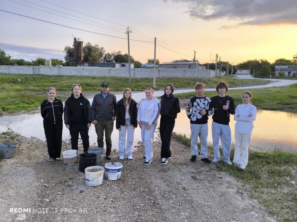 Volunteers and Mr. Victor posing with their buckets for water in front of a creek.
