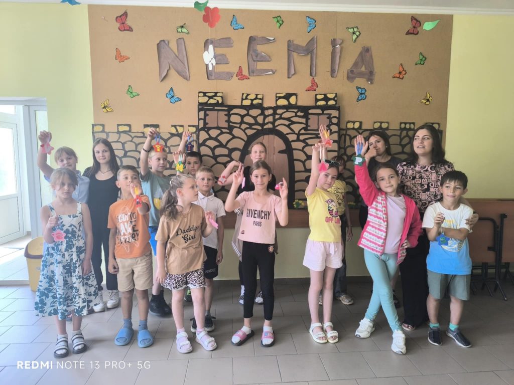 The kids with Mrs. Angela posing in fron of the word "Neemia" with showing of their crafts in their hands.