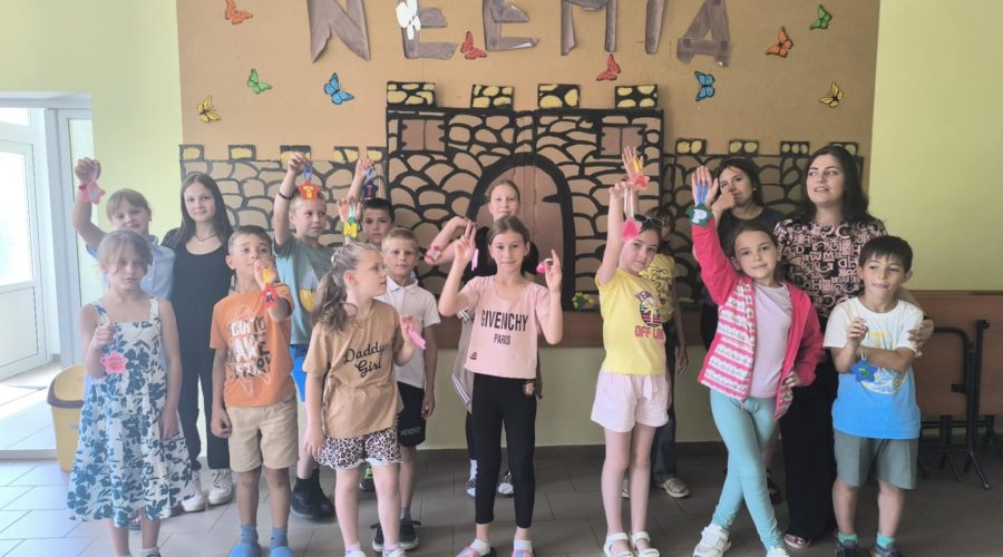The kids with Mrs. Angela posing in fron of the word "Neemia" with showing of their crafts in their hands.