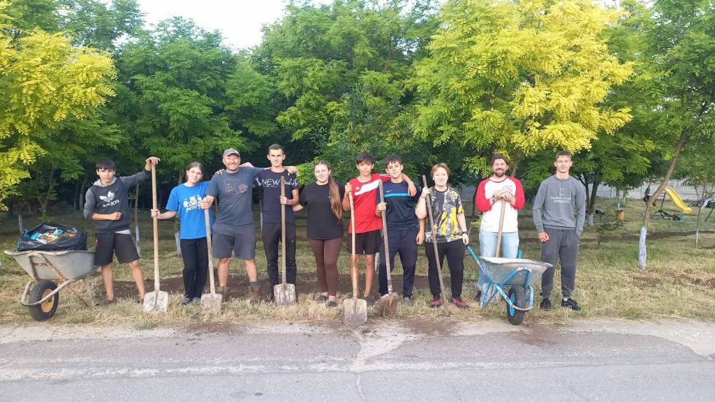 Eight youth olunteers with Victor and the Peace Corps Volunteer Adam, posing with their shovels after spreading dirt in the park.