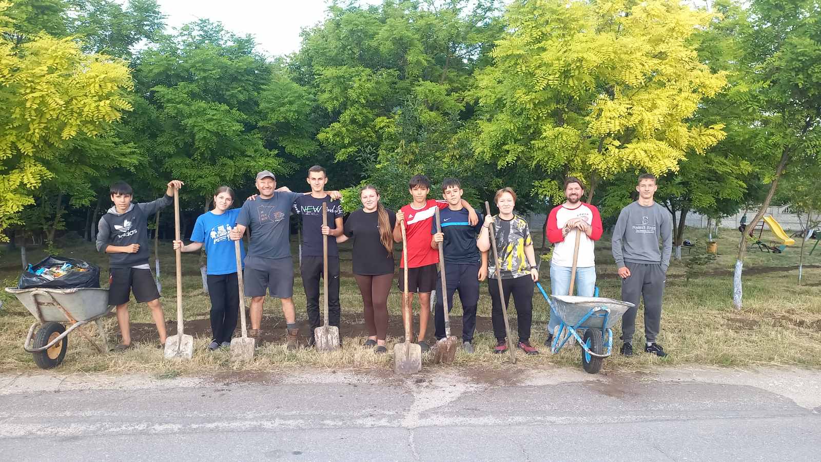 Eight youth olunteers with Victor and the Peace Corps Volunteer Adam, posing with their shovels after spreading dirt in the park.