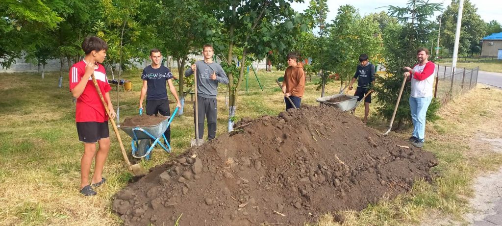 Six volunteers shoveling dirt from a giant pile.