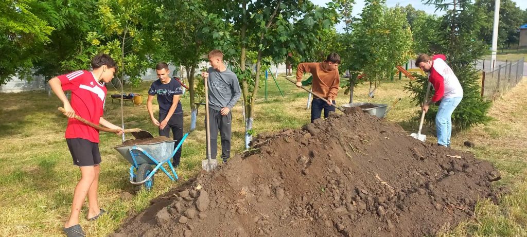 Four youth volunteers and the Peace Corps Volunteer Adam shoveling dirt from a giant pile.